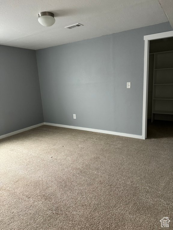 Spare room featuring carpet floors, baseboards, a textured ceiling, and visible vents