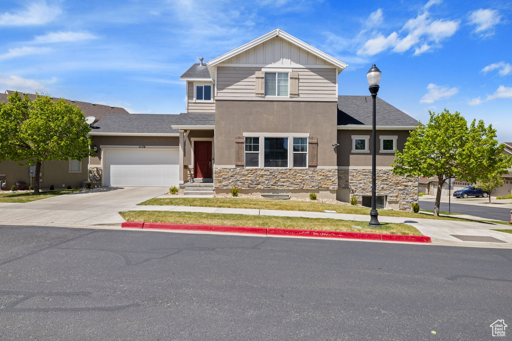 Traditional-style house with roof with shingles, stone siding, a garage, stucco siding, and concrete driveway