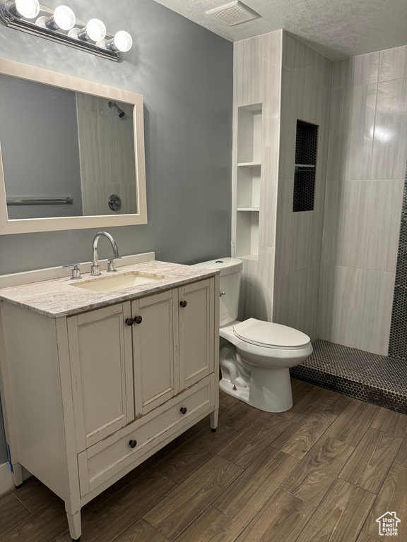 Bathroom with vanity, wood finished floors, toilet, tiled shower, and a textured ceiling
