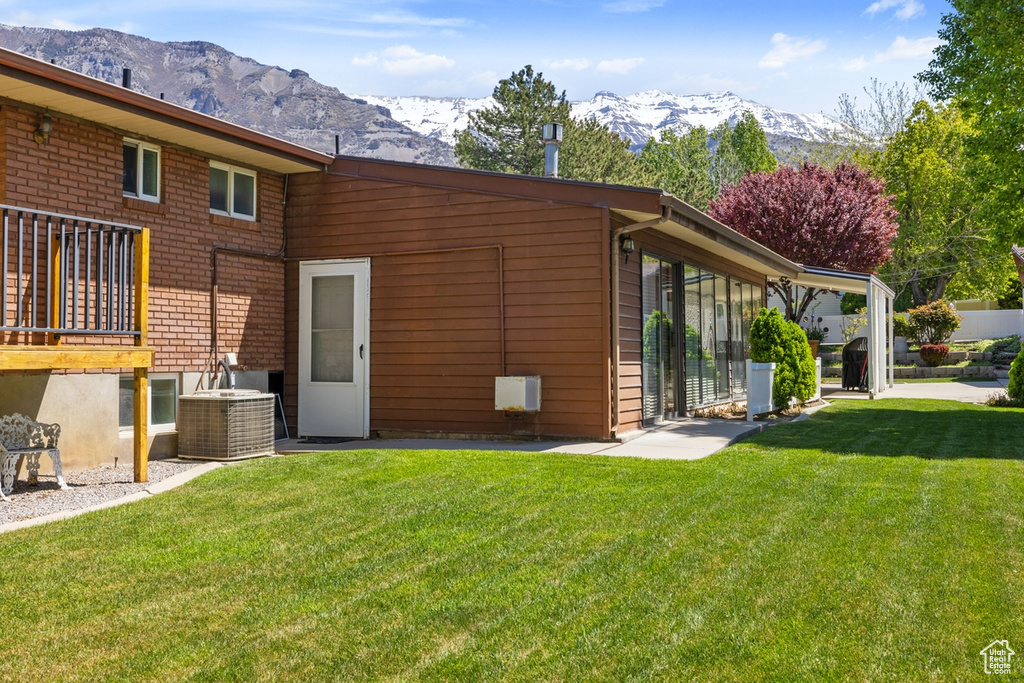 Rear view of property with central AC, a mountain view, and a yard