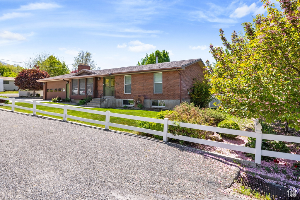 Ranch-style house with a garage, a front yard, a chimney, brick siding, and a fenced front yard