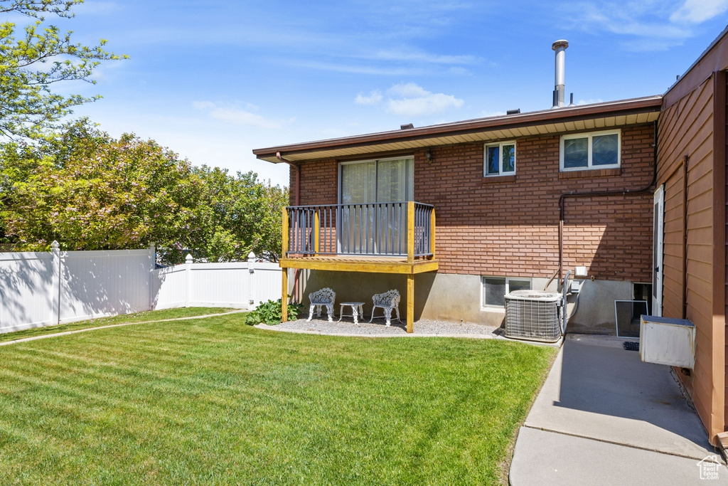 Back of house featuring a lawn, brick siding, cooling unit, and fence