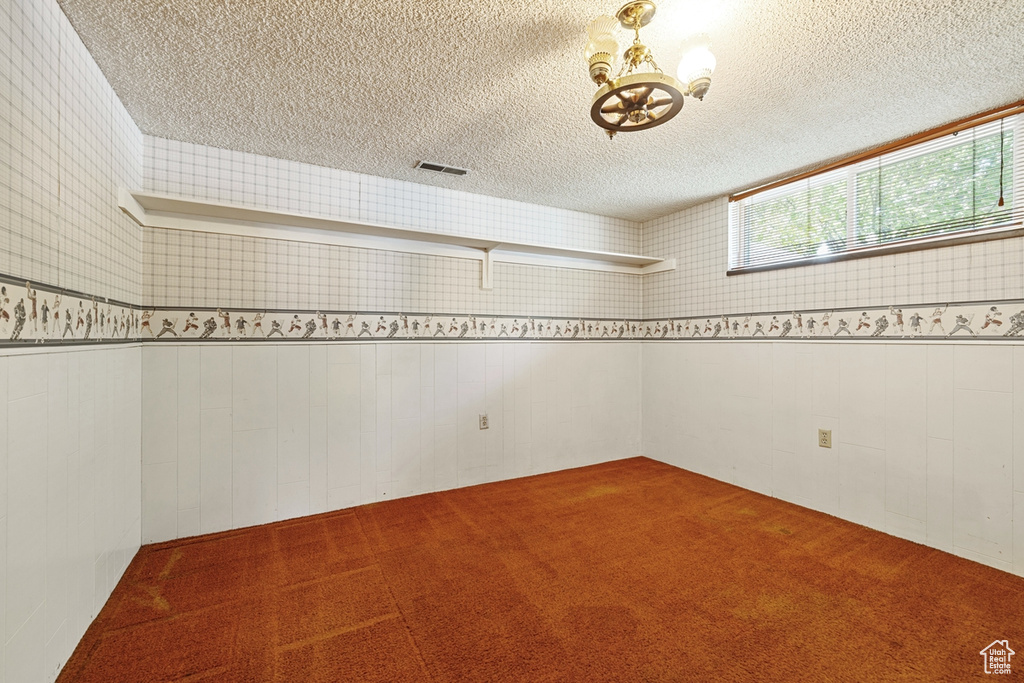 Spare room featuring visible vents, carpet, a textured ceiling, and a notable chandelier
