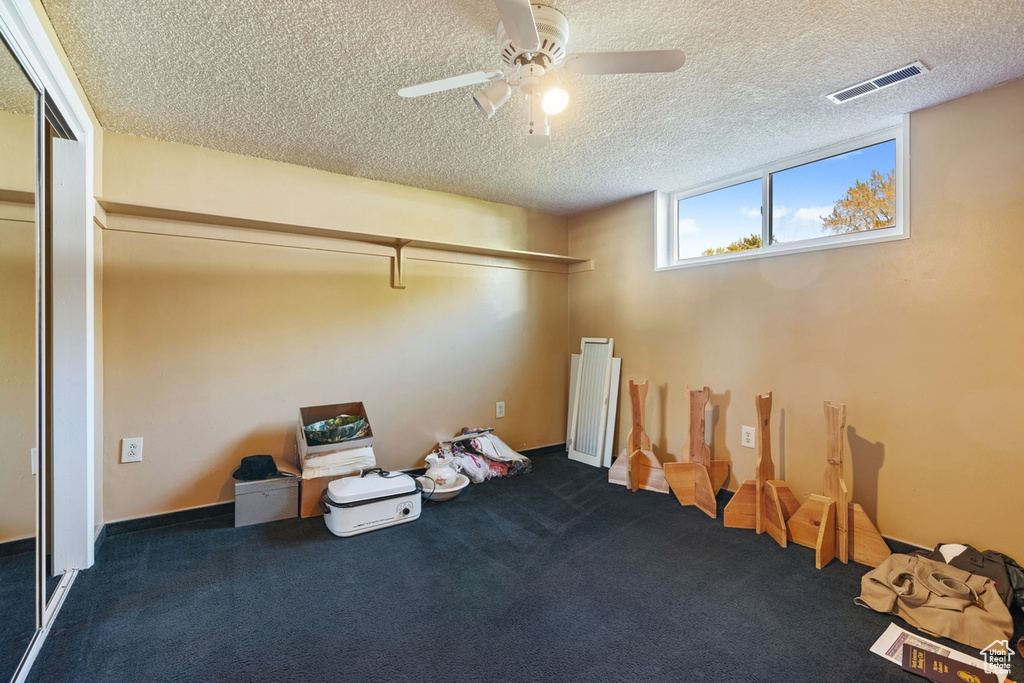 Basement featuring a ceiling fan, a textured ceiling, visible vents, and dark colored carpet