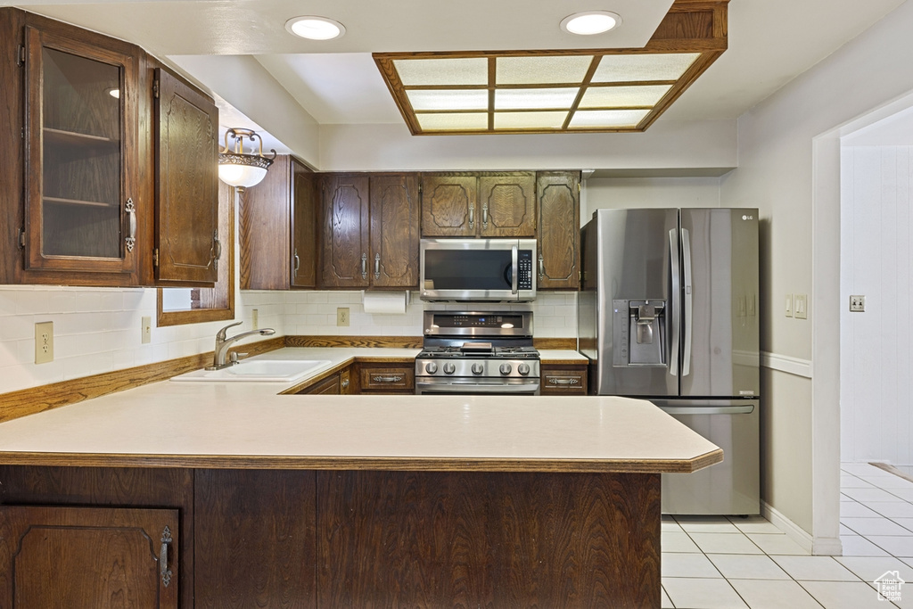 Kitchen featuring appliances with stainless steel finishes, a sink, light tile patterned floors, light countertops, and a peninsula