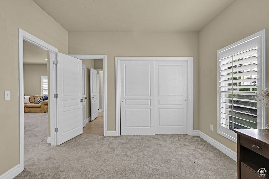Bedroom featuring light colored carpet, multiple windows, and a closet