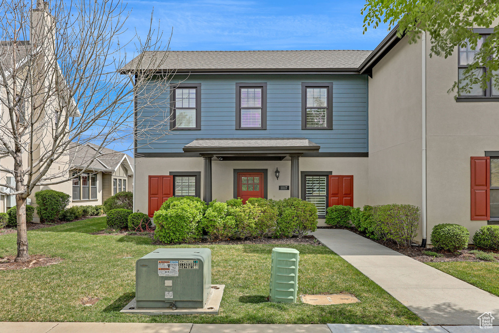 View of front of house featuring a front lawn, roof with shingles, and stucco siding