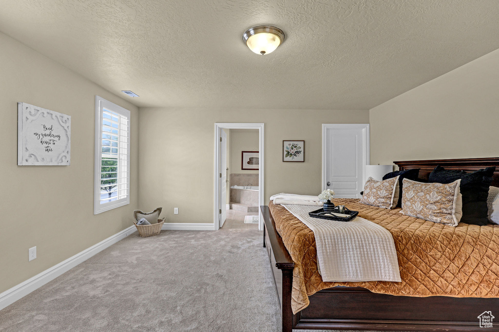 Bedroom with a textured ceiling, visible vents, carpet floors, baseboards, and ensuite bath