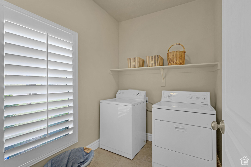 Clothes washing area featuring laundry area, baseboards, light tile patterned floors, and washing machine and clothes dryer