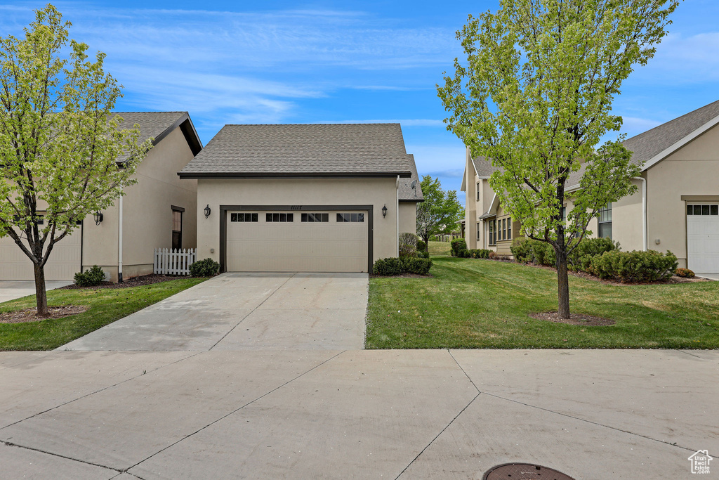 View of front of property with concrete driveway, an attached garage, stucco siding, and a front lawn