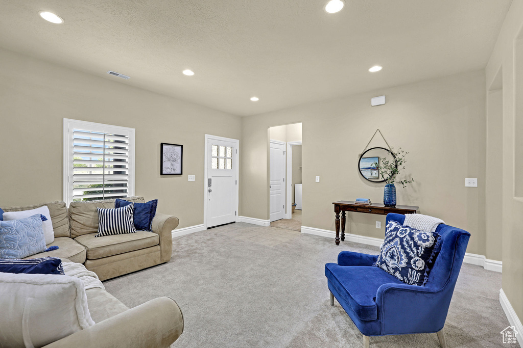 Living area with light colored carpet, visible vents, and a healthy amount of sunlight