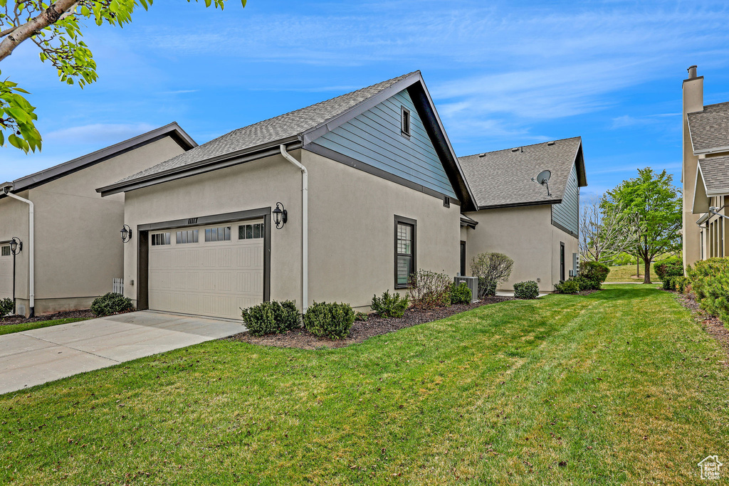 View of side of home with a garage, stucco siding, concrete driveway, central air condition unit, and a yard