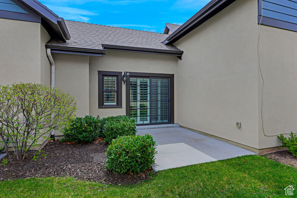 Entrance to property featuring a patio, roof with shingles, and stucco siding