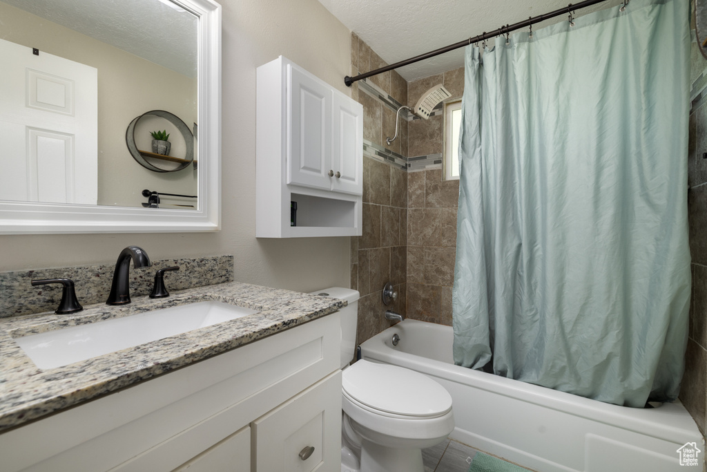 Full bath with vanity, a textured ceiling, toilet, and shower / tub combo