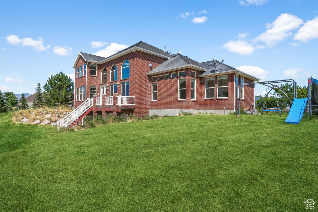 Back of house featuring a yard, a playground, and brick siding