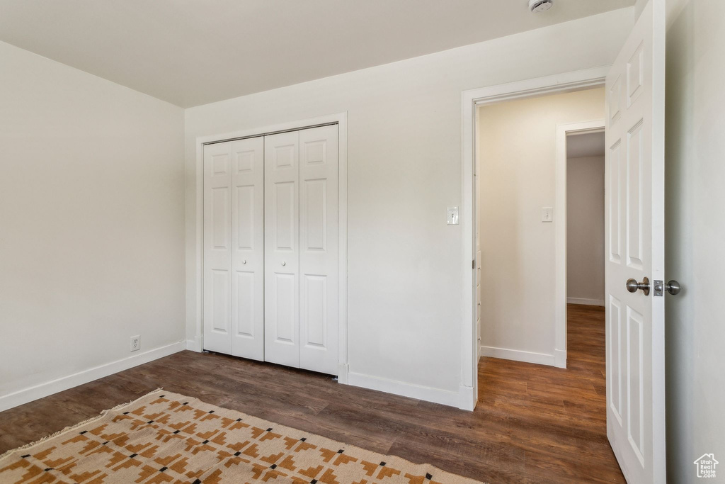 Unfurnished bedroom featuring baseboards, a closet, and dark wood-type flooring