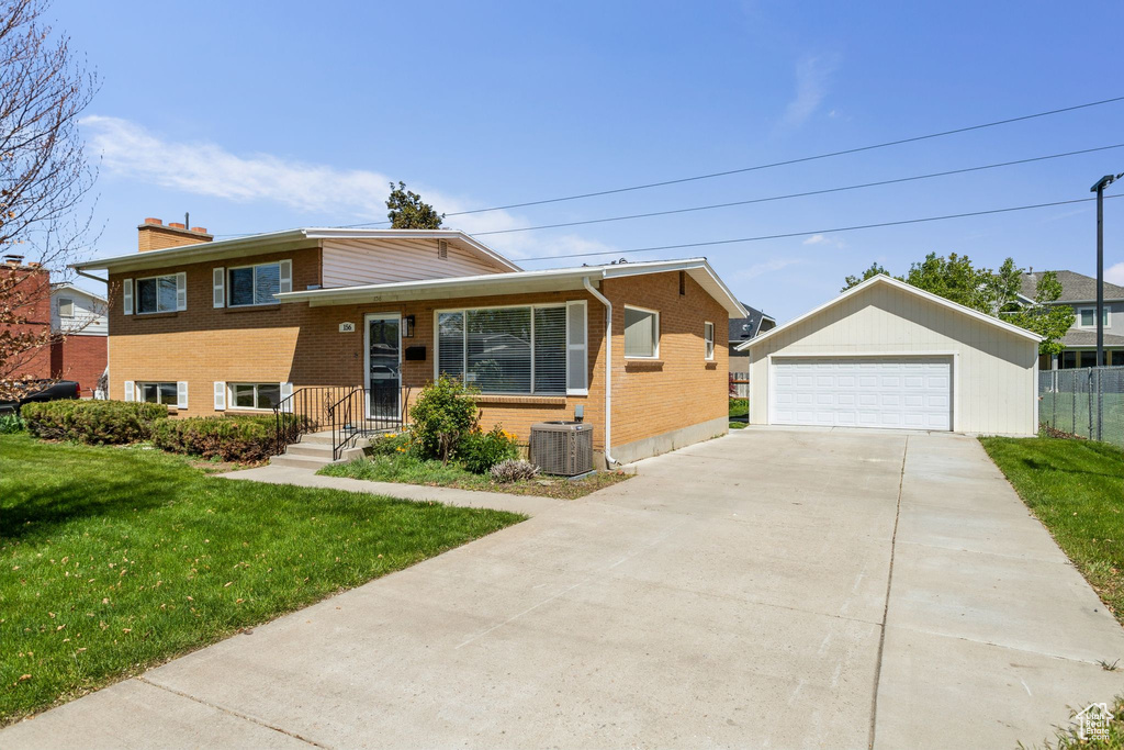 Split level home with a chimney, a front yard, an outbuilding, a garage, and brick siding
