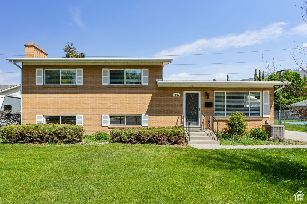 Split level home with central AC unit, a chimney, a front yard, and brick siding