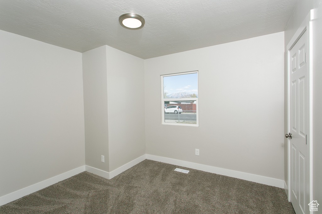 Unfurnished room featuring a textured ceiling, baseboards, visible vents, and dark colored carpet