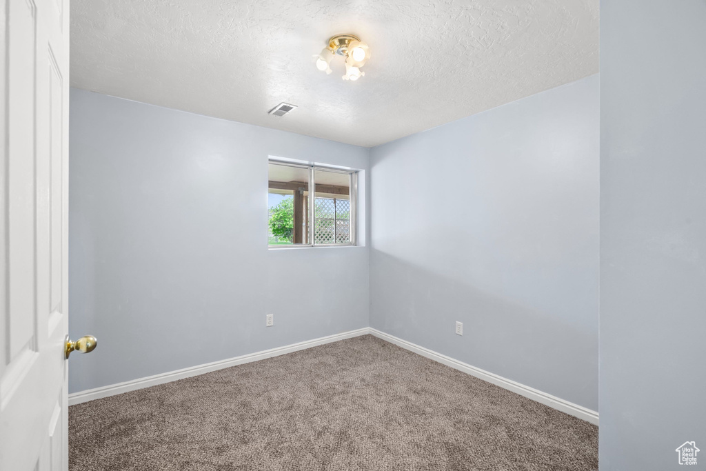 Carpeted empty room featuring visible vents, a textured ceiling, and baseboards
