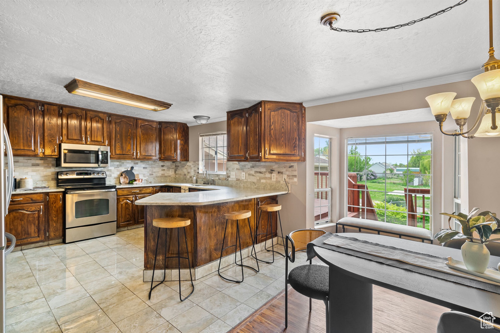 Kitchen with light countertops, a textured ceiling, stainless steel appliances, a peninsula, and decorative backsplash