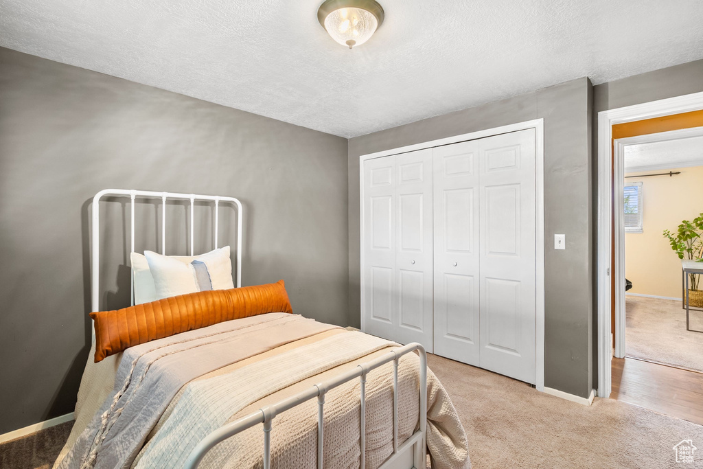 Bedroom featuring light colored carpet, a textured ceiling, baseboards, and a closet