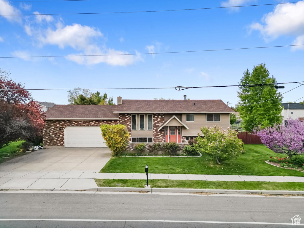 View of front facade with driveway, a front yard, a garage, brick siding, and fence