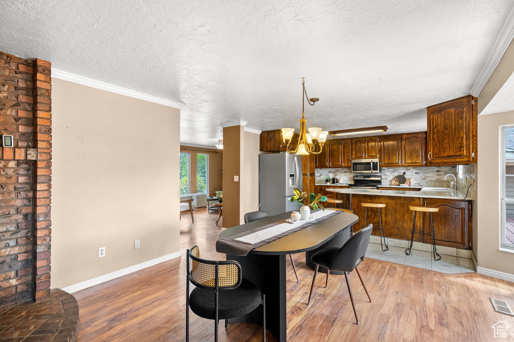 Dining room with light wood-style floors, a textured ceiling, baseboards, and a chandelier