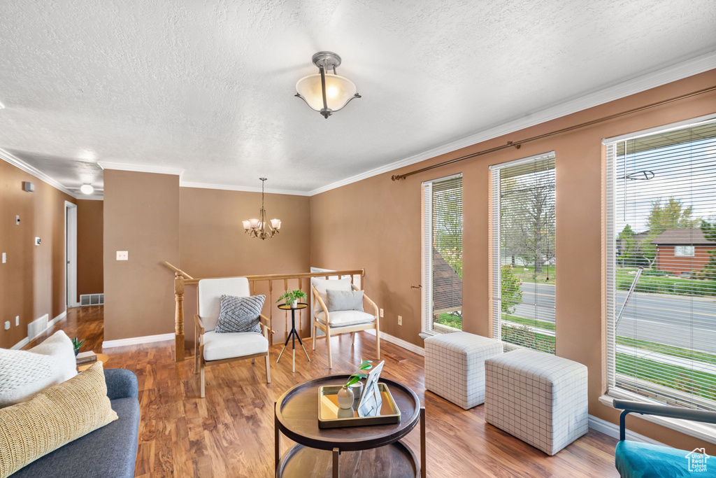 Living area featuring a textured ceiling, a chandelier, ornamental molding, and wood finished floors