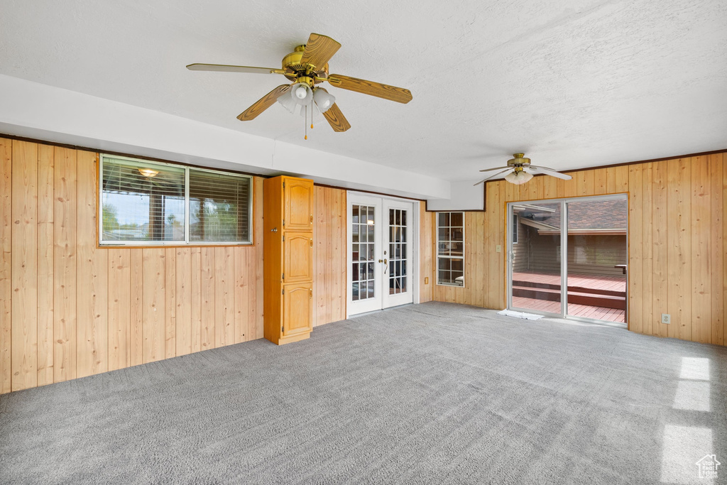 Carpeted spare room with a ceiling fan, french doors, and wood walls