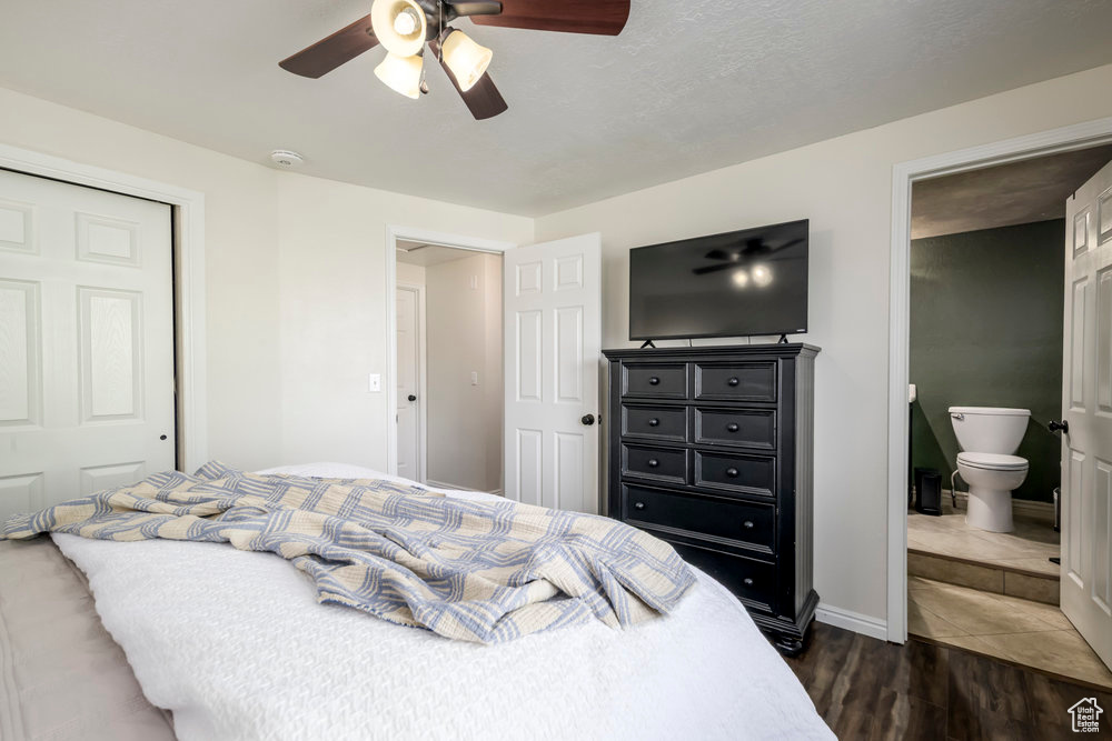 Bedroom featuring a closet, dark wood-style flooring, baseboards, a ceiling fan, and ensuite bath