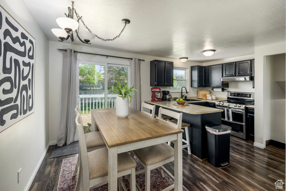 Kitchen featuring dark wood-style flooring, a peninsula, light countertops, under cabinet range hood, and double oven range