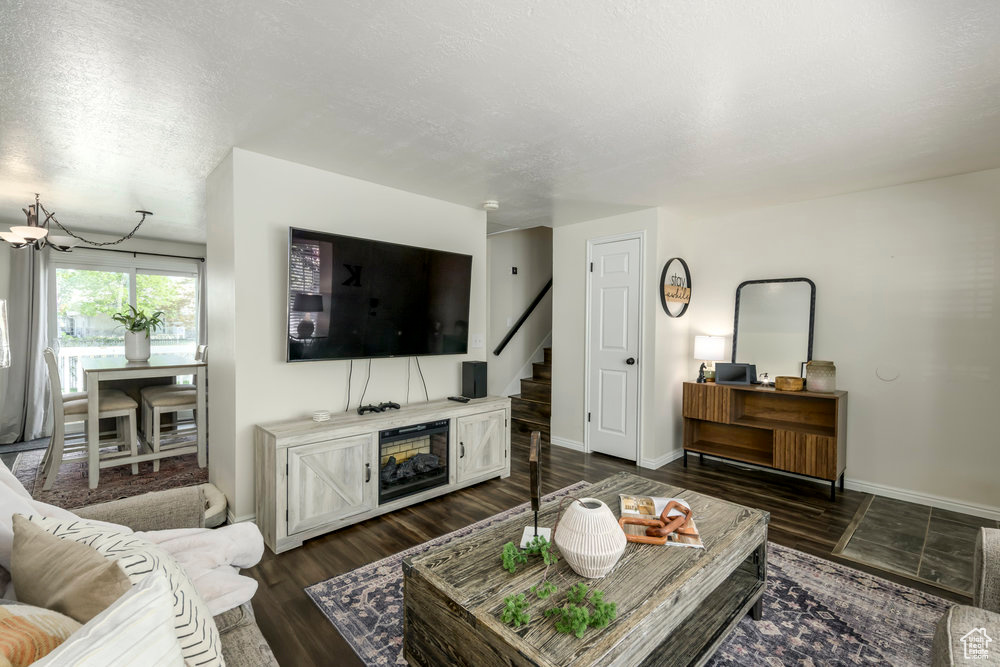 Living room with stairs, baseboards, dark wood-style floors, a textured ceiling, and a chandelier