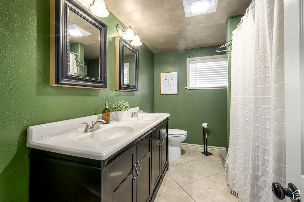 Bathroom with a sink, tile patterned floors, a textured wall, and toilet