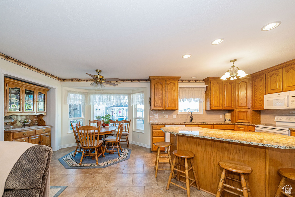 Kitchen with brown cabinetry, a breakfast bar area, white appliances, and tasteful backsplash
