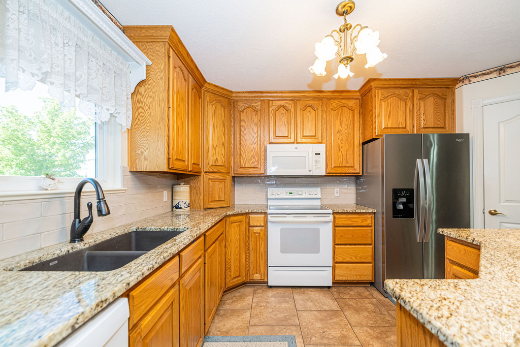 Kitchen featuring backsplash, a sink, light stone counters, a notable chandelier, and white appliances