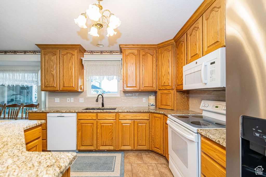 Kitchen featuring a sink, white appliances, a chandelier, brown cabinetry, and backsplash