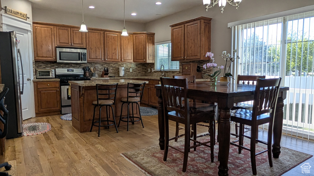 Kitchen featuring a kitchen island, backsplash, brown cabinets, stainless steel appliances, and light wood-style flooring