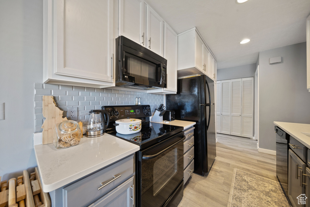 Kitchen featuring light wood-style floors, light countertops, white cabinetry, decorative backsplash, and black appliances