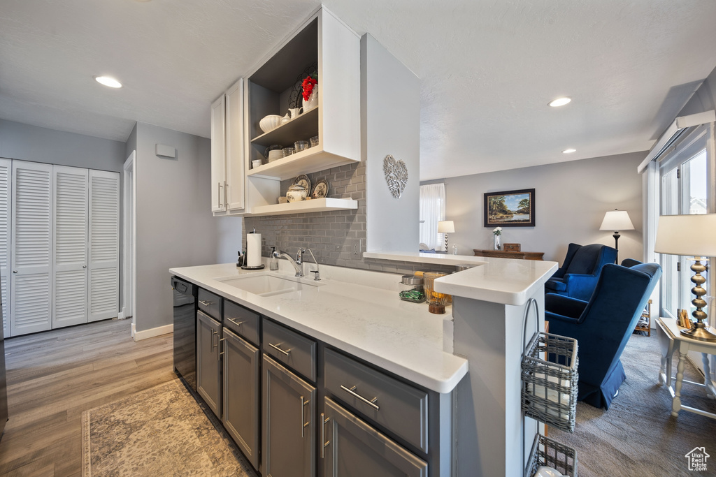 Kitchen with open shelves, black dishwasher, light countertops, tasteful backsplash, and a sink