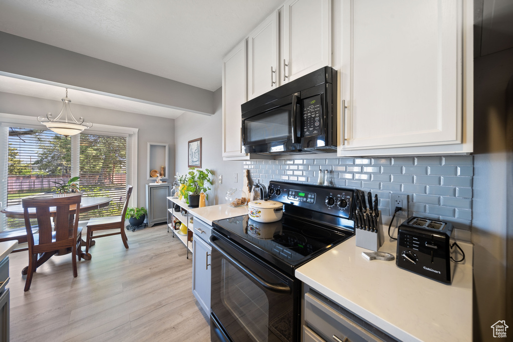 Kitchen with light countertops, white cabinetry, black appliances, and tasteful backsplash