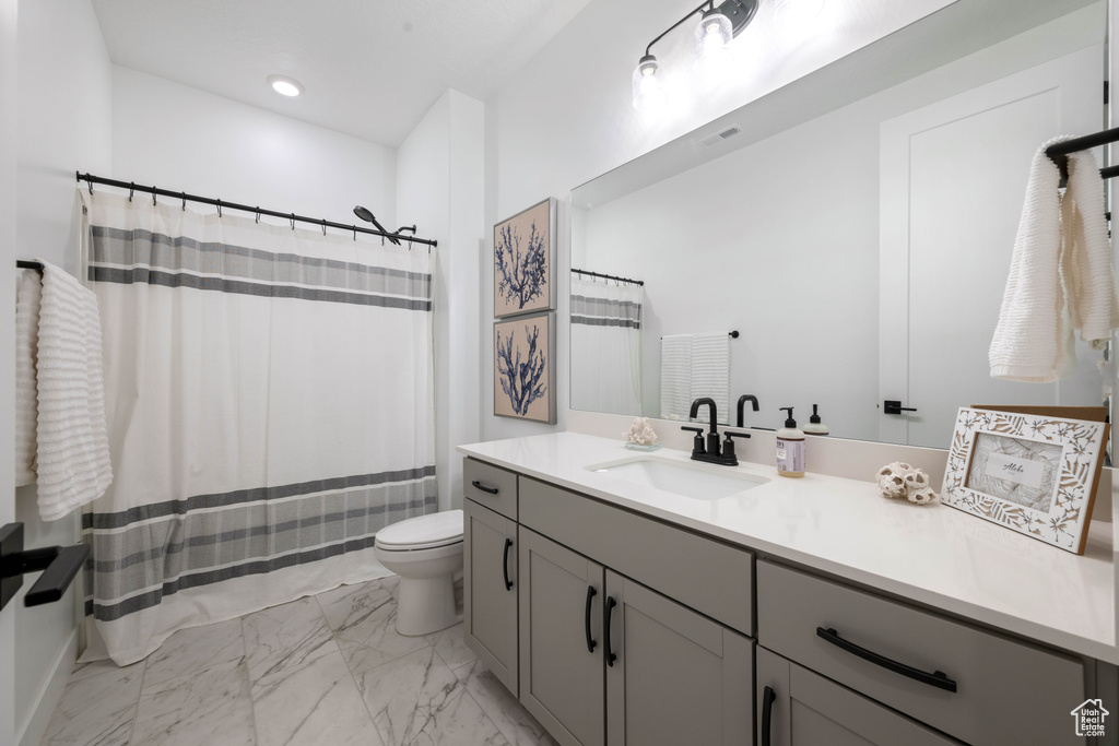 Bathroom featuring toilet, curtained shower, marble finish floor, and vanity