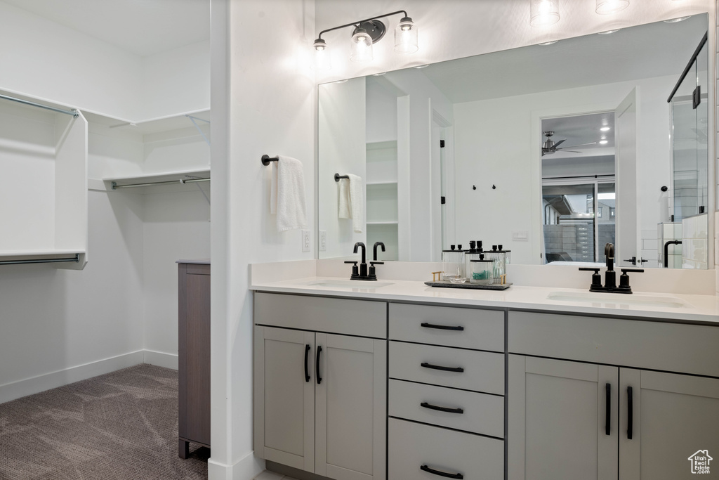 Ensuite bathroom with double vanity, baseboards, ceiling fan, and a sink