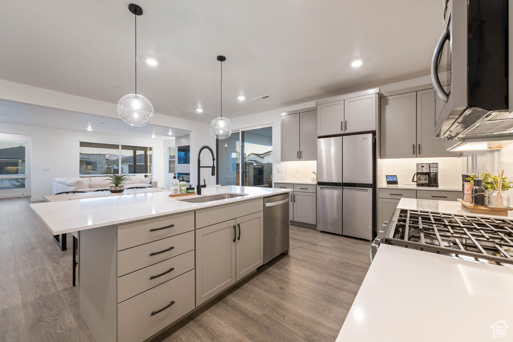 Kitchen with gray cabinets, appliances with stainless steel finishes, a sink, light countertops, and light wood finished floors