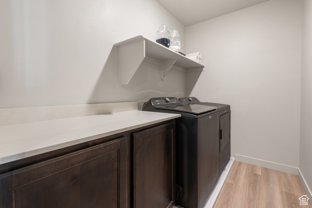 Laundry room with washer and dryer, baseboards, cabinet space, and light wood-style floors