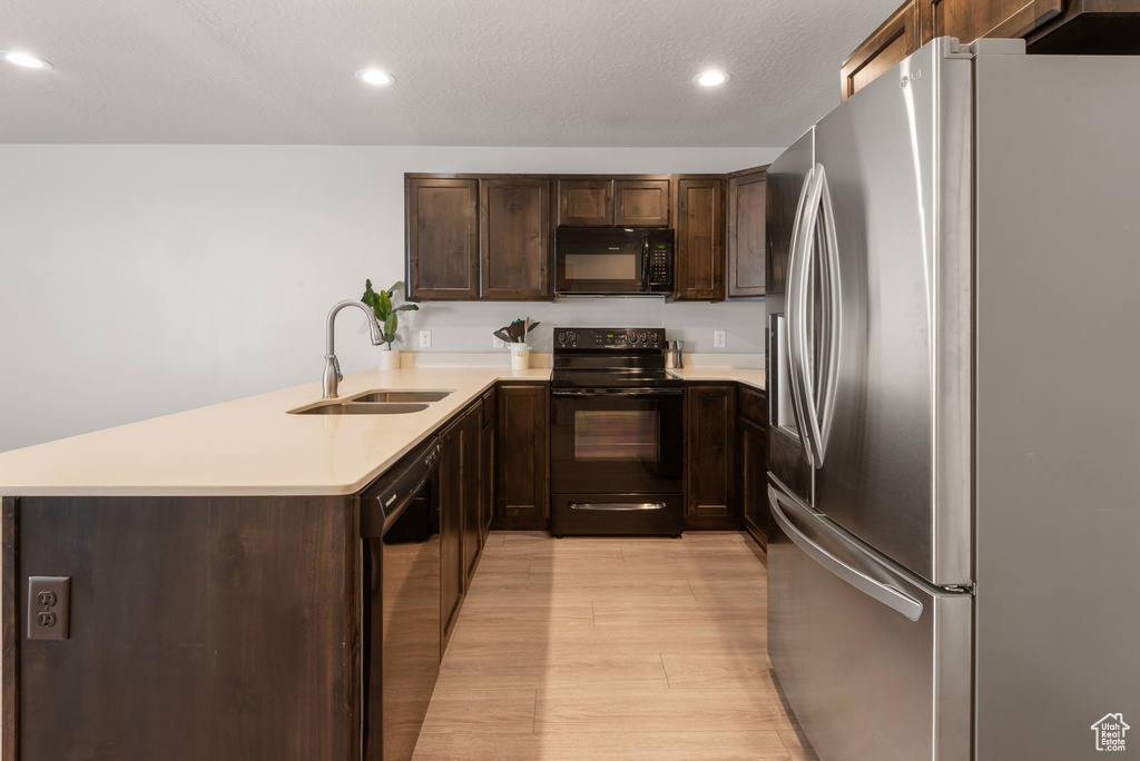 Kitchen with dark brown cabinetry, light wood-type flooring, a sink, light countertops, and black appliances