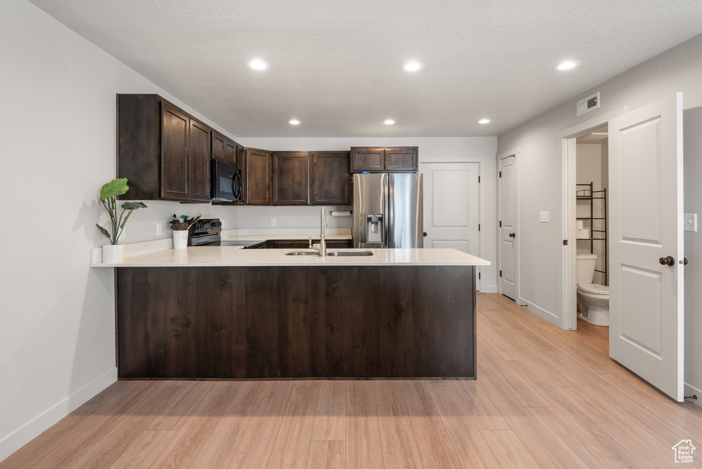 Kitchen with range with electric stovetop, stainless steel refrigerator with ice dispenser, visible vents, black microwave, and a sink