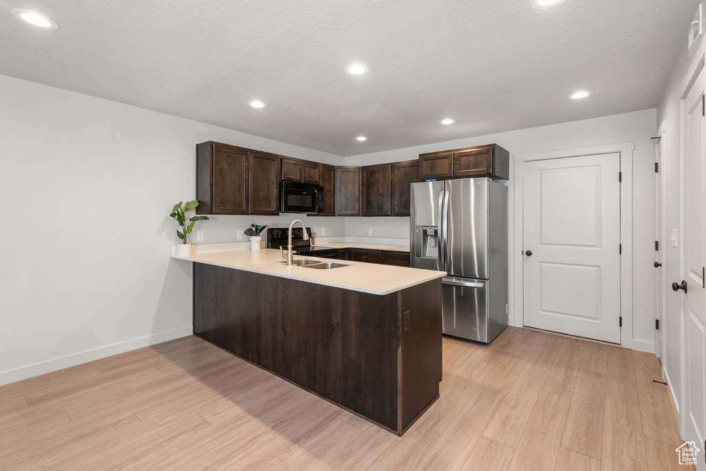 Kitchen featuring dark brown cabinets, black microwave, light countertops, a peninsula, and stainless steel refrigerator with ice dispenser