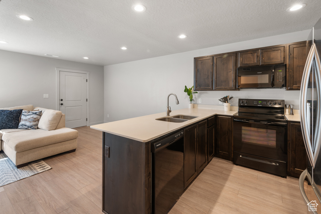 Kitchen featuring light wood-type flooring, a sink, light countertops, black appliances, and open floor plan