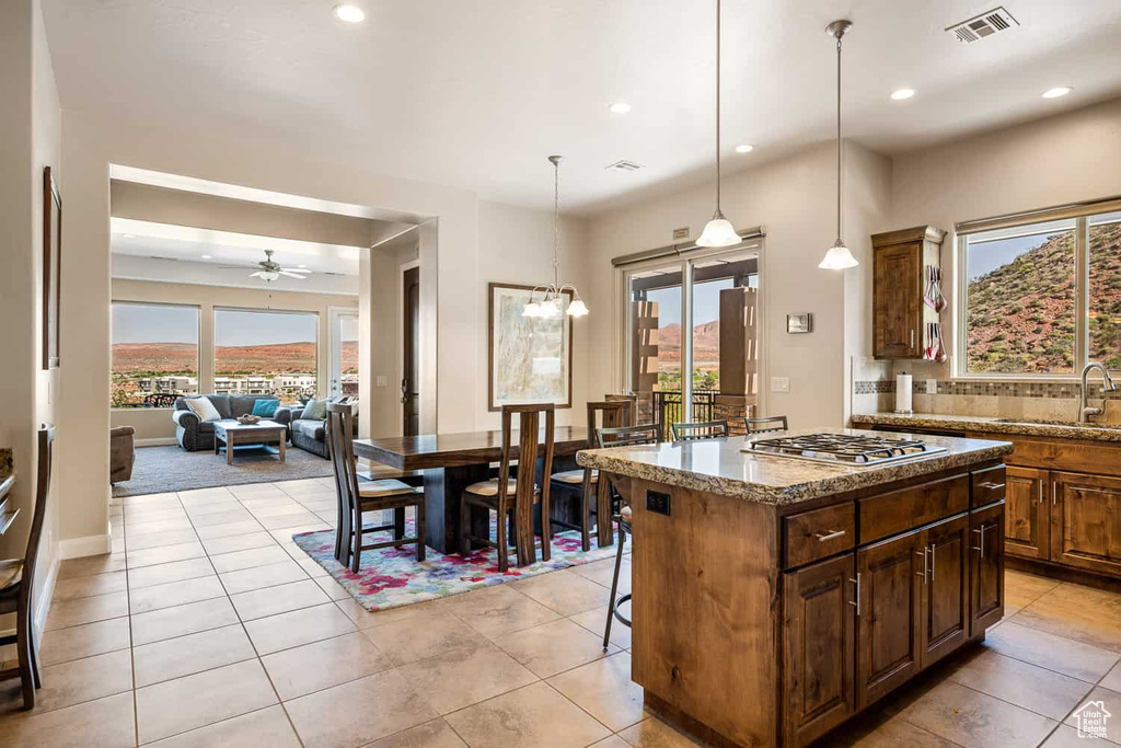 Kitchen with a kitchen island, visible vents, a sink, light stone counters, and stainless steel gas stovetop